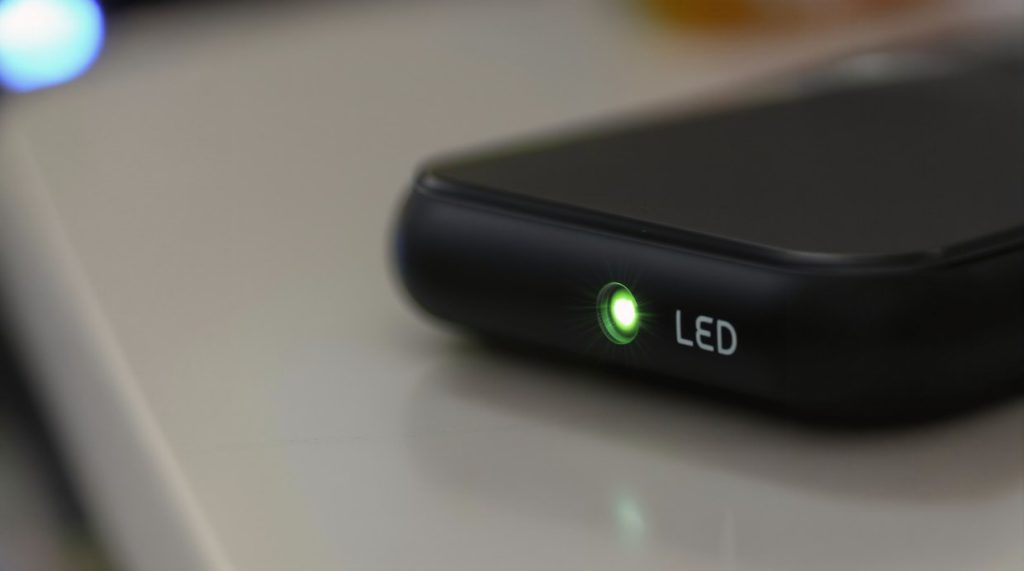 Macro close-up of a single green activity LED glowing on a black plastic device casing in deep blurry shadow